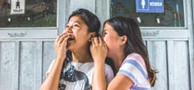 Two teenage girls whisper and laugh to eachother