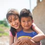 A boy crouches on the ground and smiles up at the camera