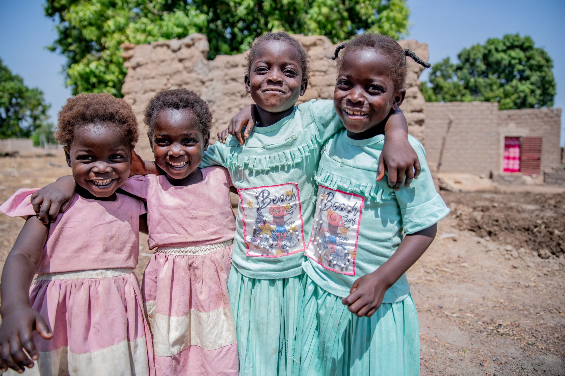 Four smiling girls standing outside with arms around each other's shoulders.