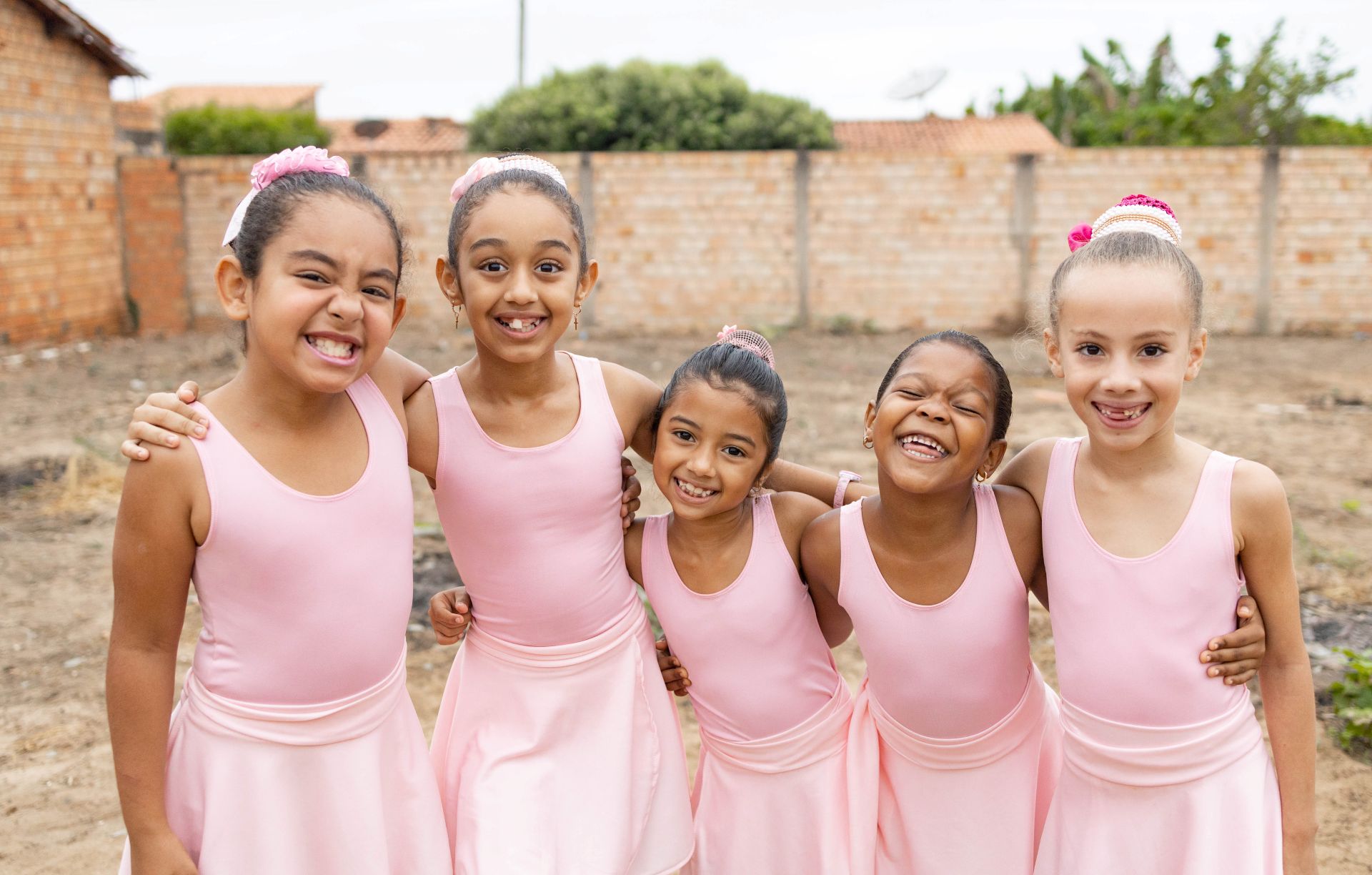 Five girls in pink leotards are standing together posing for a picture with their arms around each other. They take dance classes at the center.