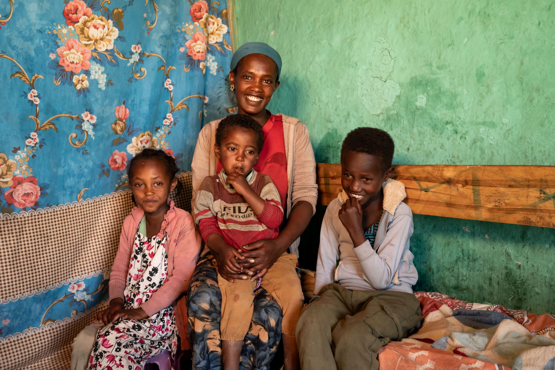 A smiling mother sits with her three children in her home, the youngest child on her lap.