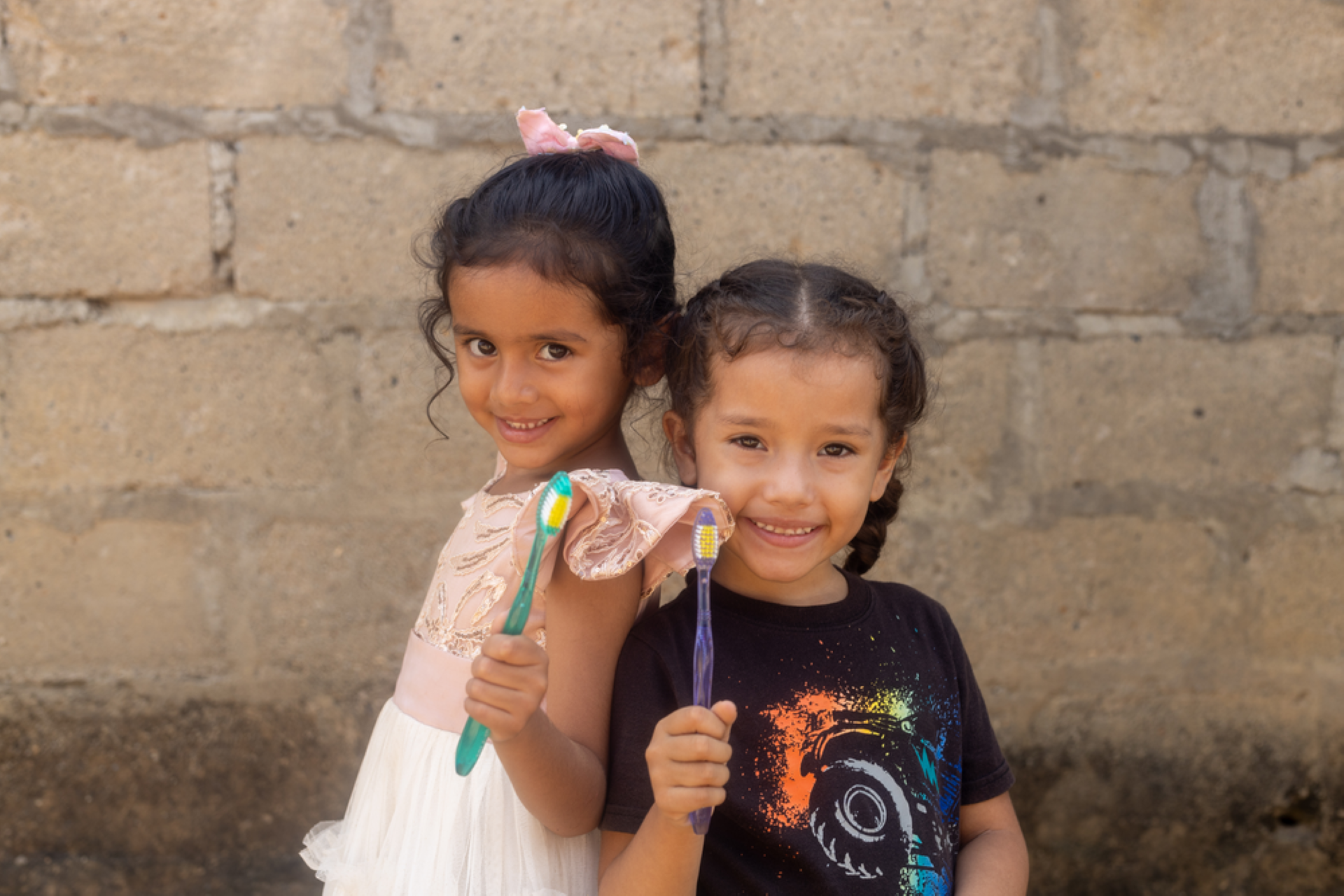 Two little girls holding toothbrushes are smiling into the camera.