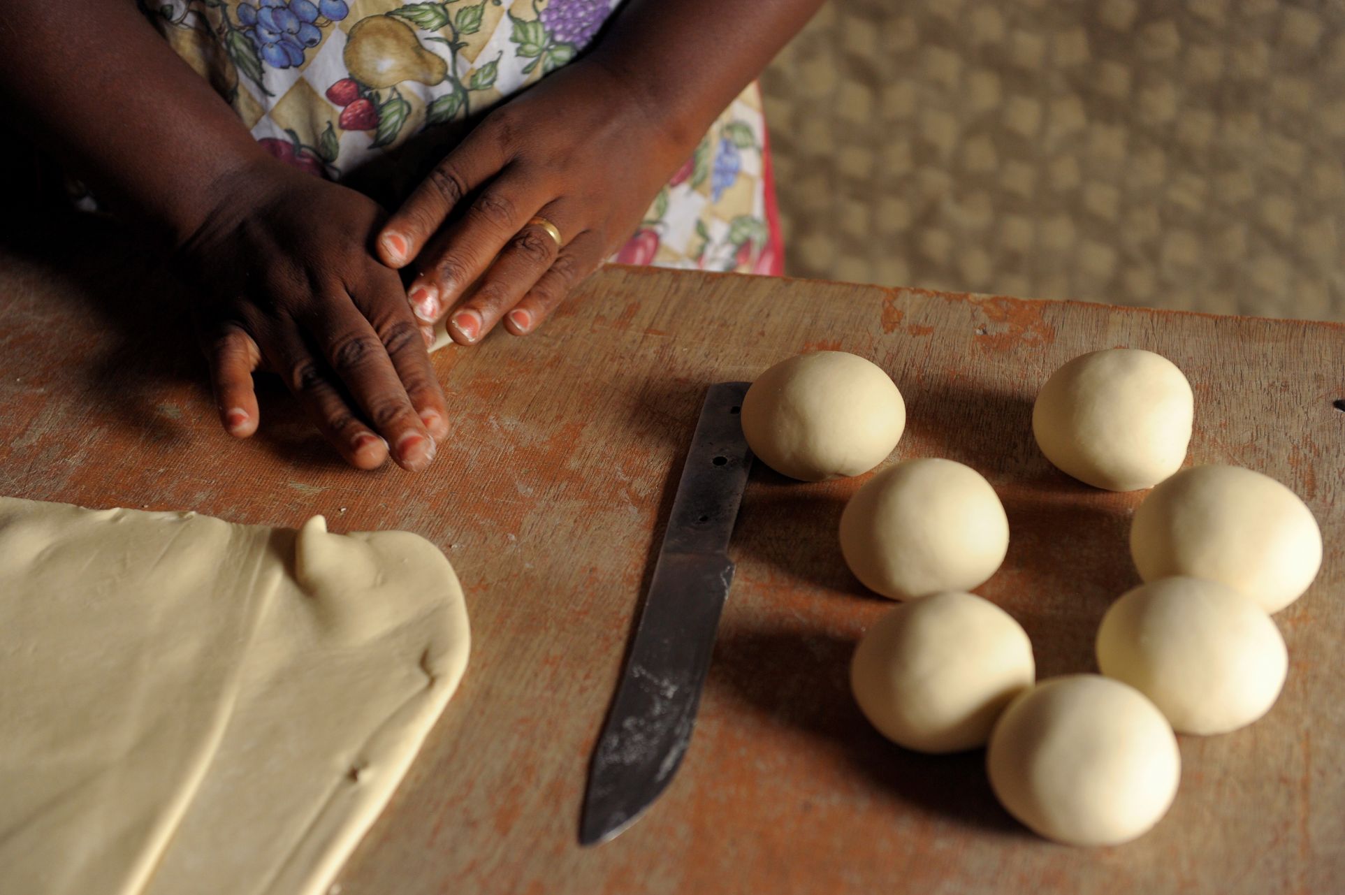 Photo of hands rolling dough on a wooden table with a knife.