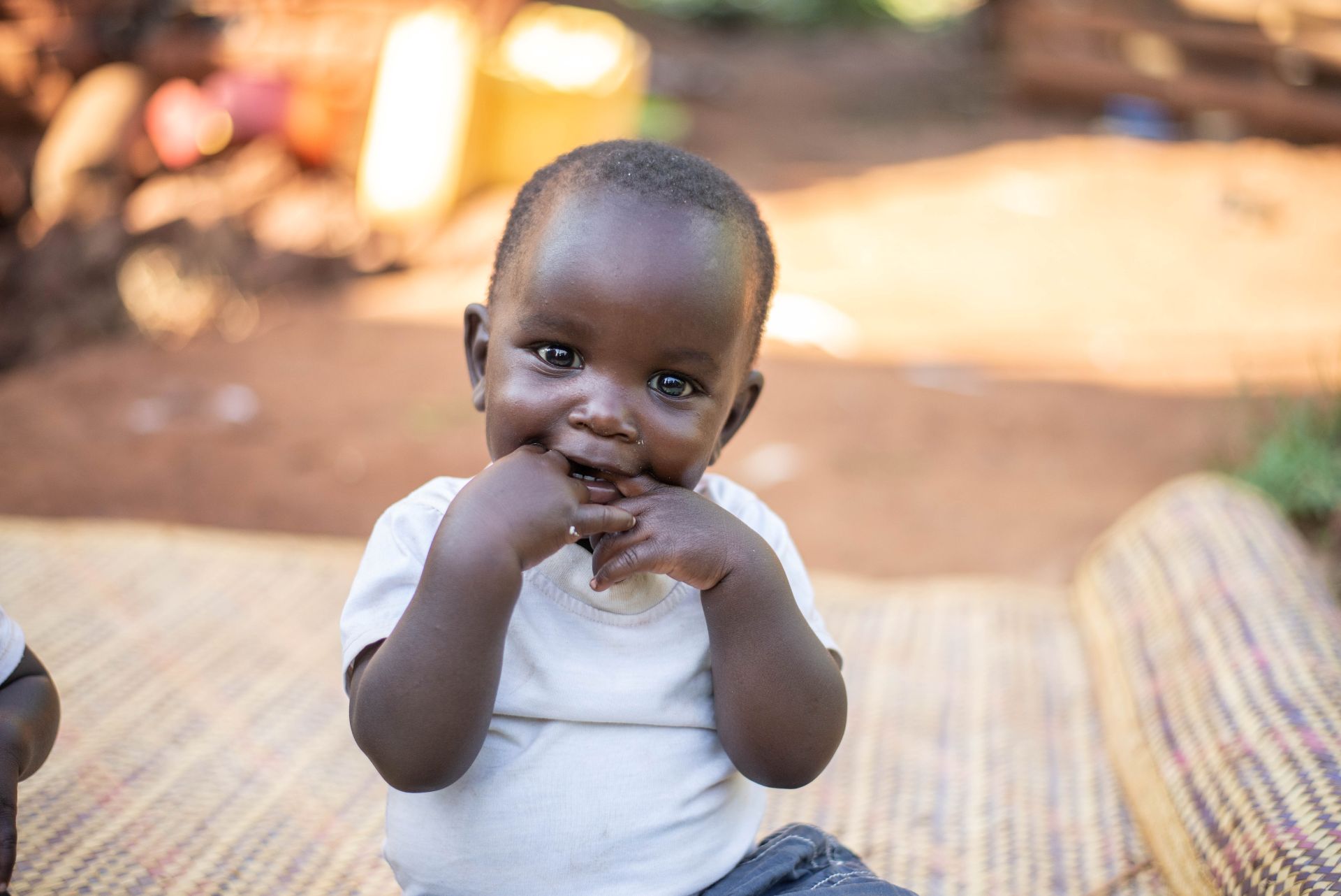 Beautiful baby boy sitting up and smiling, looking into the camera while chewing on his own fingers.