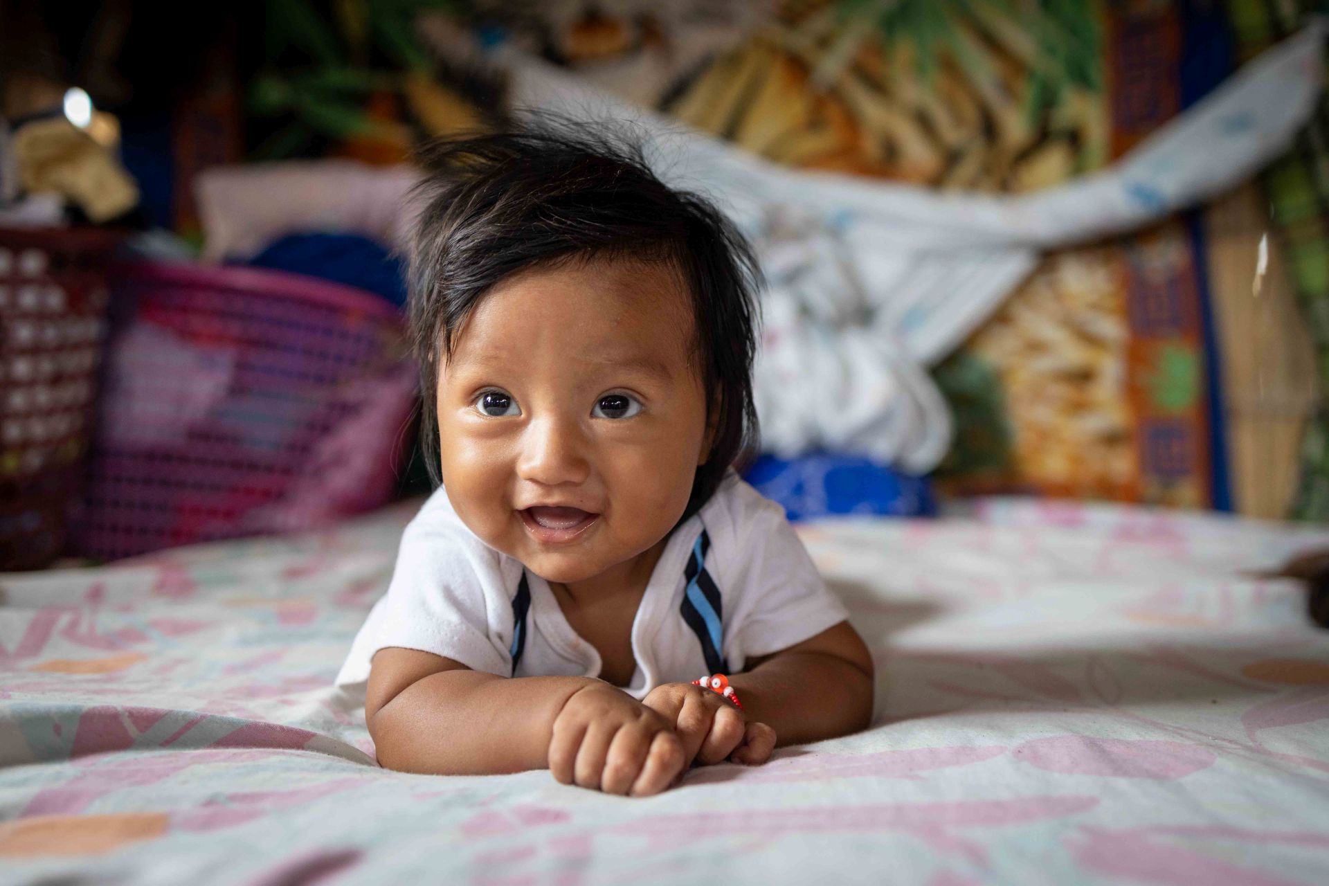 Smiling baby is laying on his tummy on a bed.