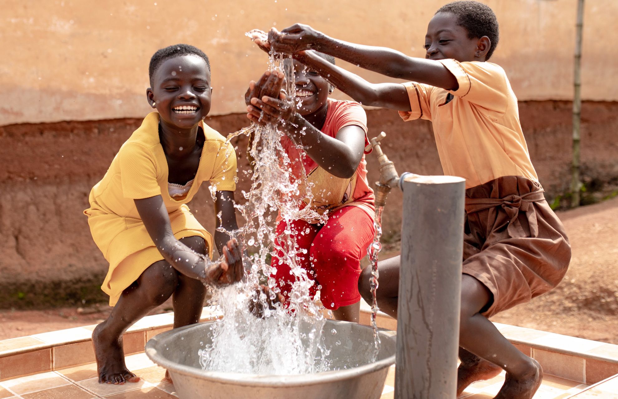 Three smiling children play outside in sparkling water pouring from a tap with their cupped hands.