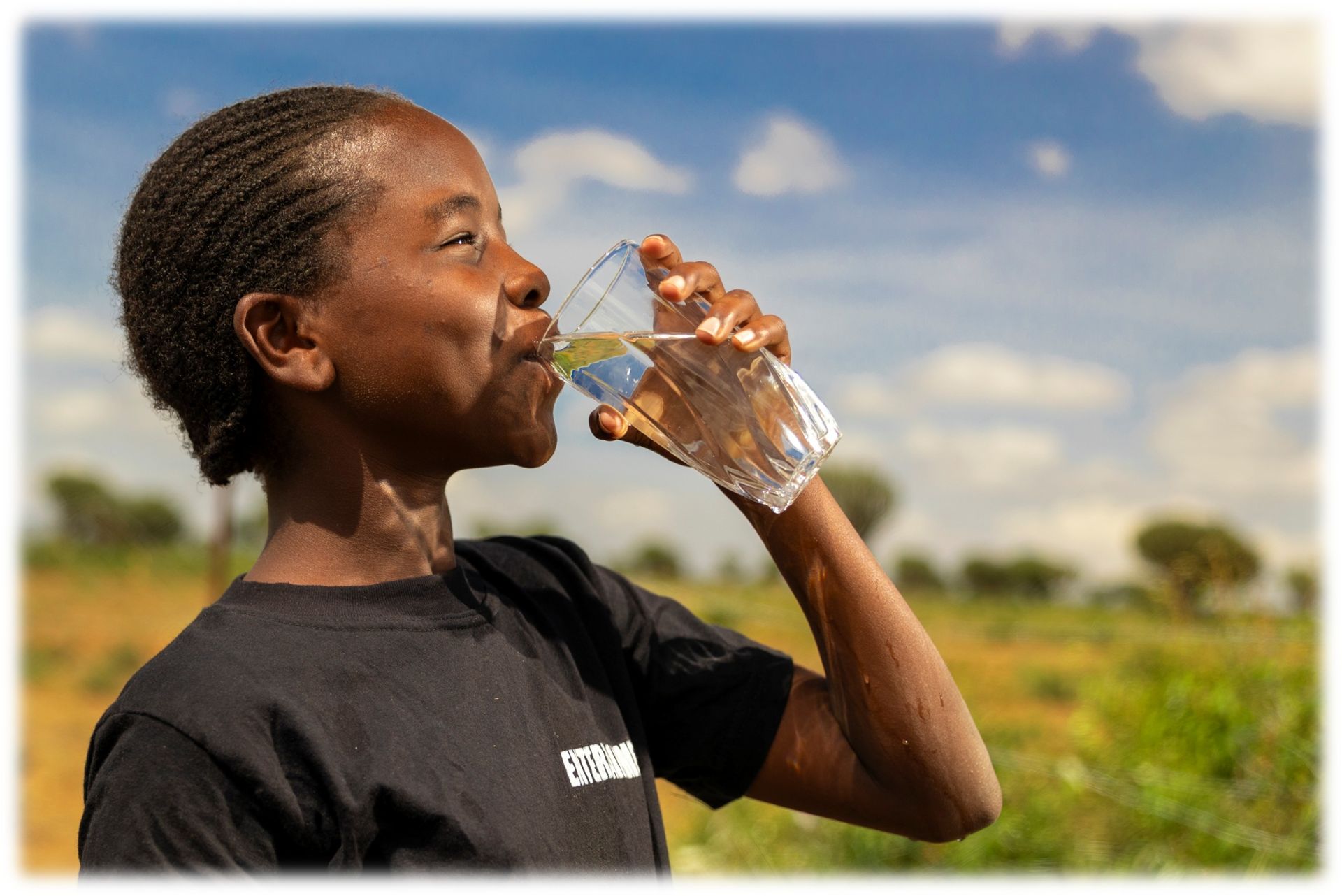 Side profile of a boy drinking clean water from a glass outdoors.