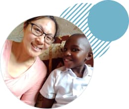 Andrea sits next to her sponsored child and smiles. She's visited his home on a sponsor trip.