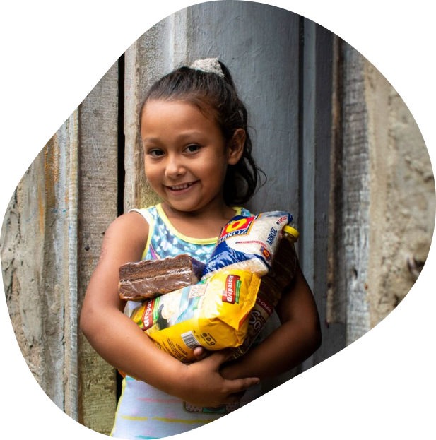 A girl stands outside holding a care package of food delivered by Compassion