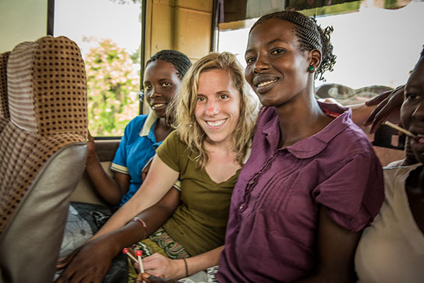 A visitor sits on a mini bus with some local friends. They smile and hold hands.